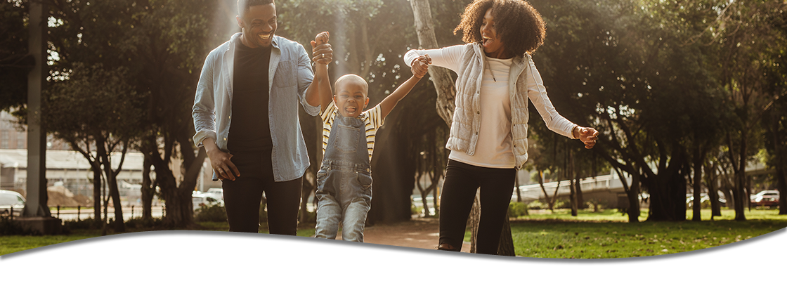 Family walking in park together, swinging child between two parents.