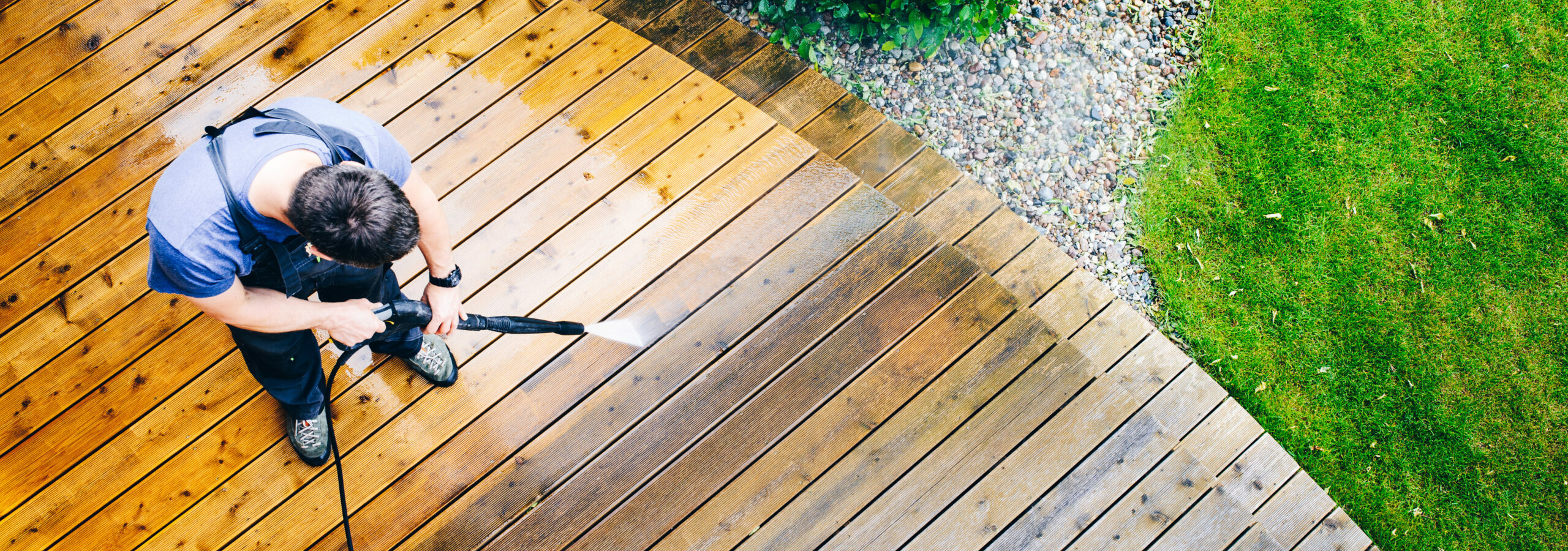 Man powerwashing a wooden deck in a back patio.