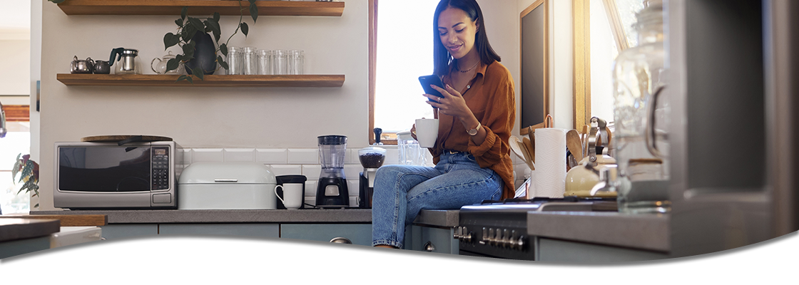 woman sitting on counter reading on phone, drinking coffee