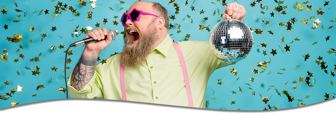 Man holding a disco ball and singing into a microphone with confetti in the background.