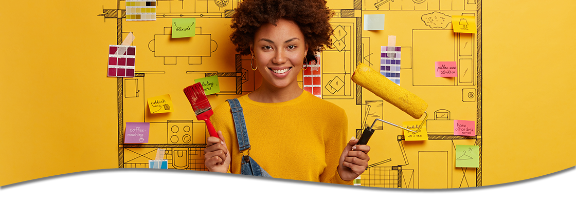 Woman with paint brush and roller standing in front of a blueprint of a house.