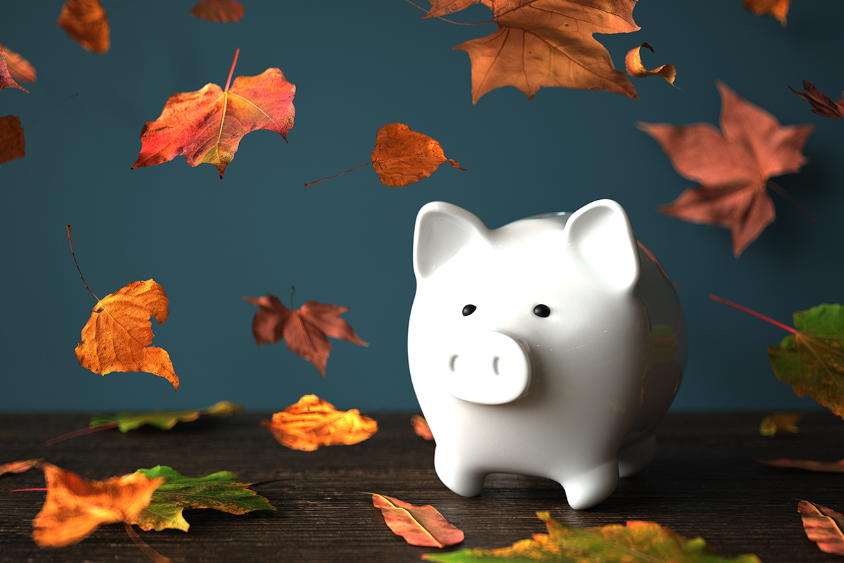 white piggy bank among falling autumn leaves